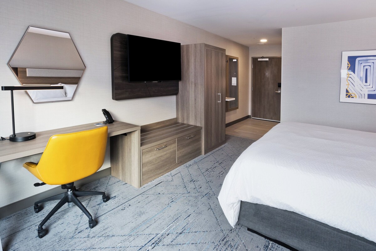 A hotel room with a bed, a desk with a chair, a television, and a wardrobe.