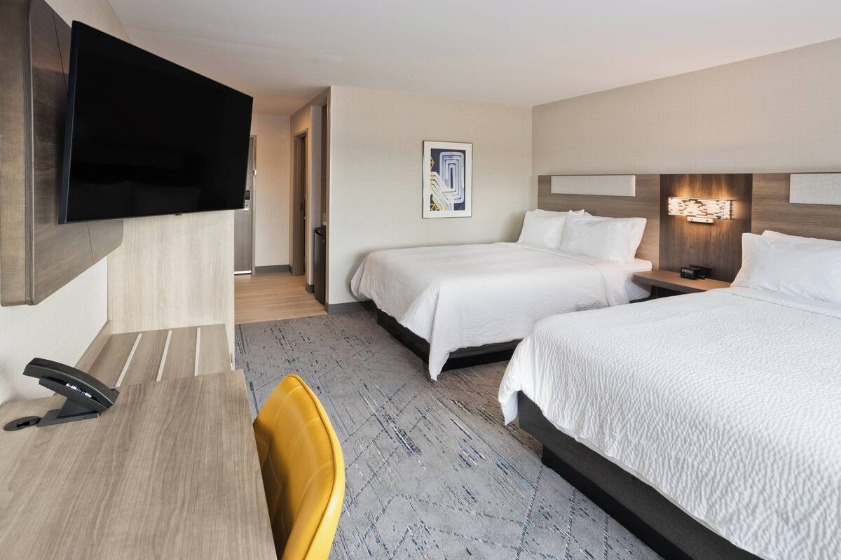 A hotel room with two beds, a desk, a chair, a flat-screen TV, and a painting on the wall.