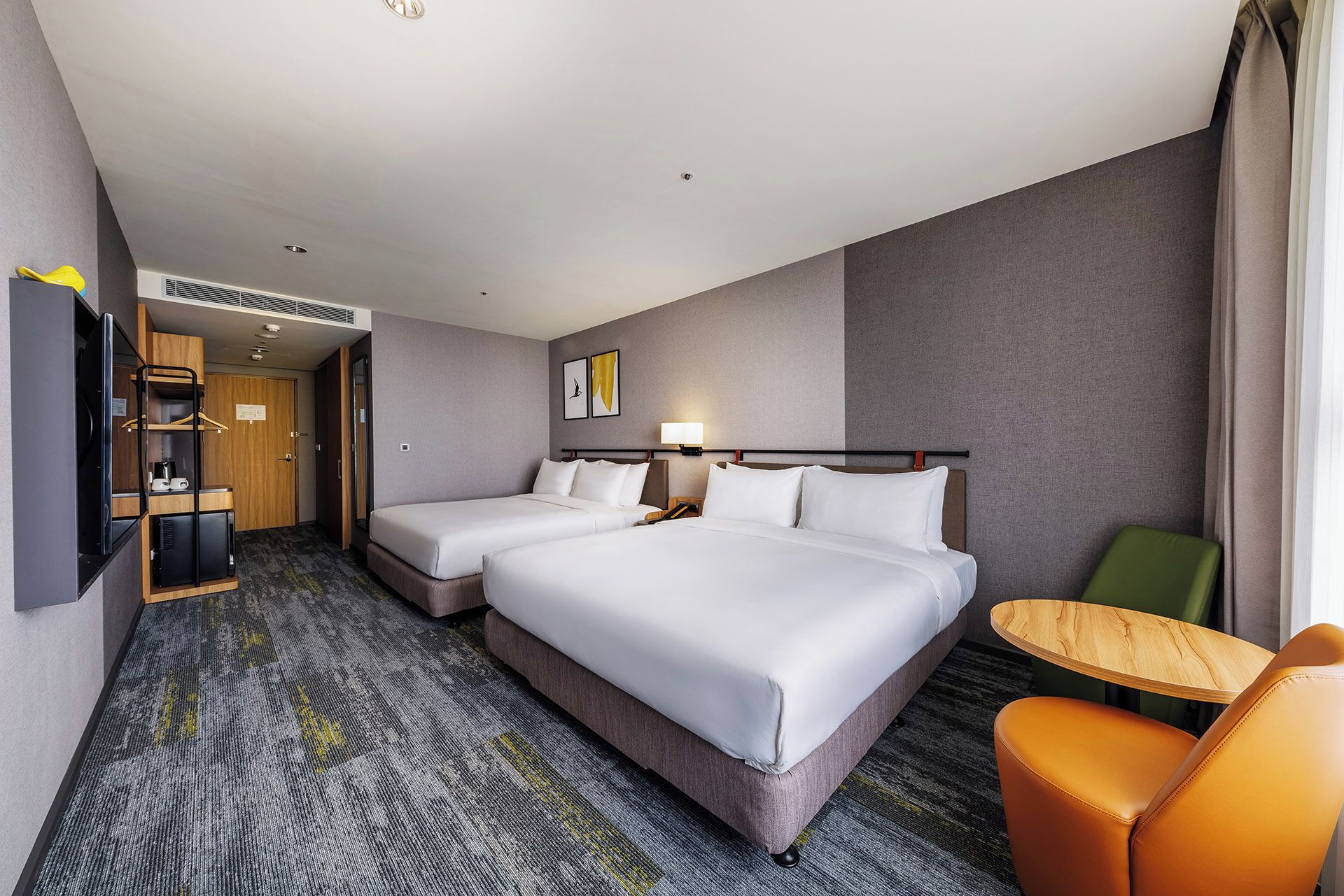 A hotel room with two beds, a desk, a chair, and a small table.