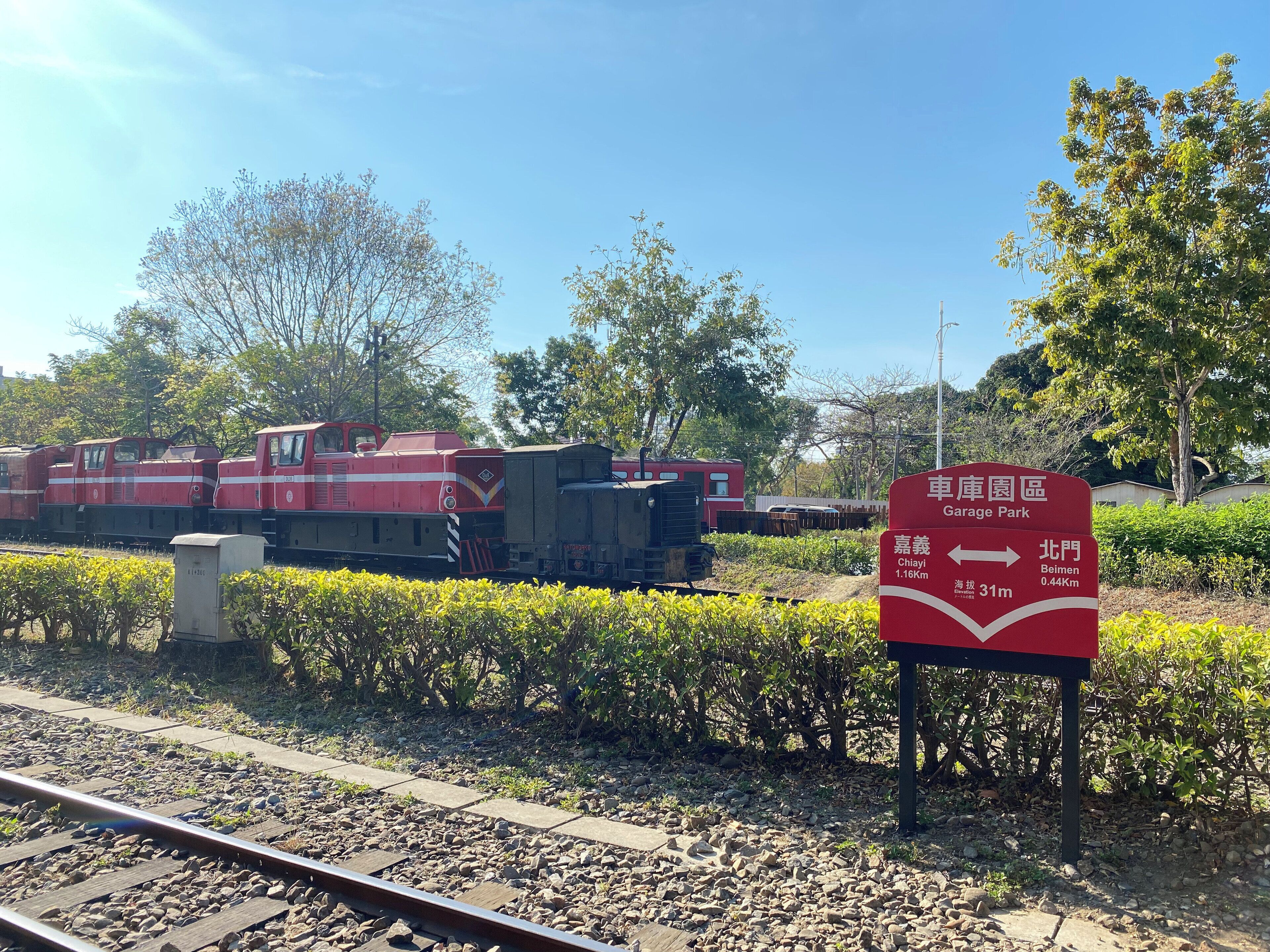 Une gare avec un train rouge et un panneau indiquant les directions vers Chiayi et Beimen.