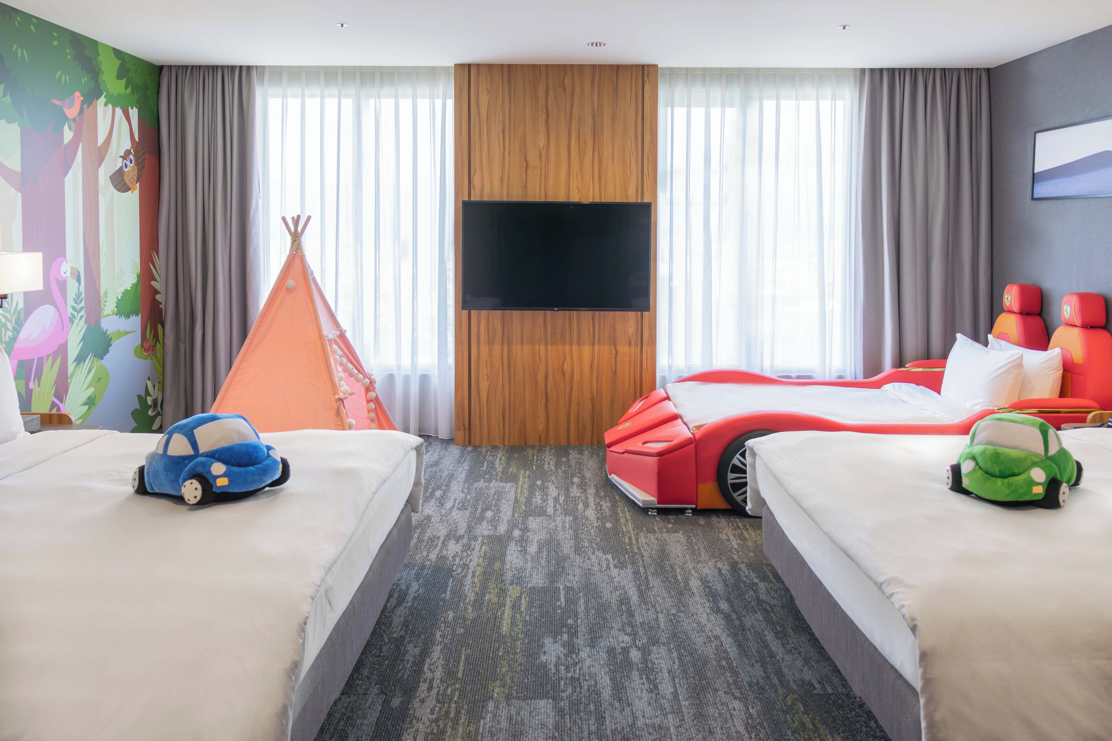 Hotellihuone, jossa on kaksi sänkyä, suuri televisio, puupanelilla verhoiltu seinä ja metsäteemainen seinämaalaus.