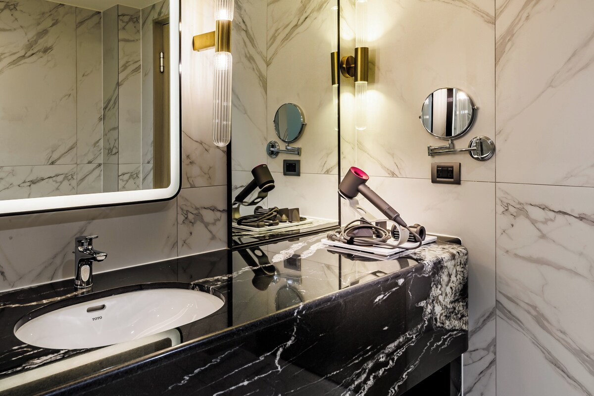 A modern bathroom with a marble sink, a large mirror, and a towel rack.