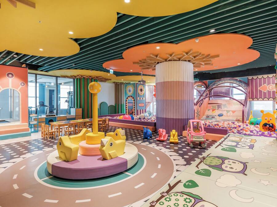 A children's play area with colorful play structures, a large central column, and a play mat with animal designs.