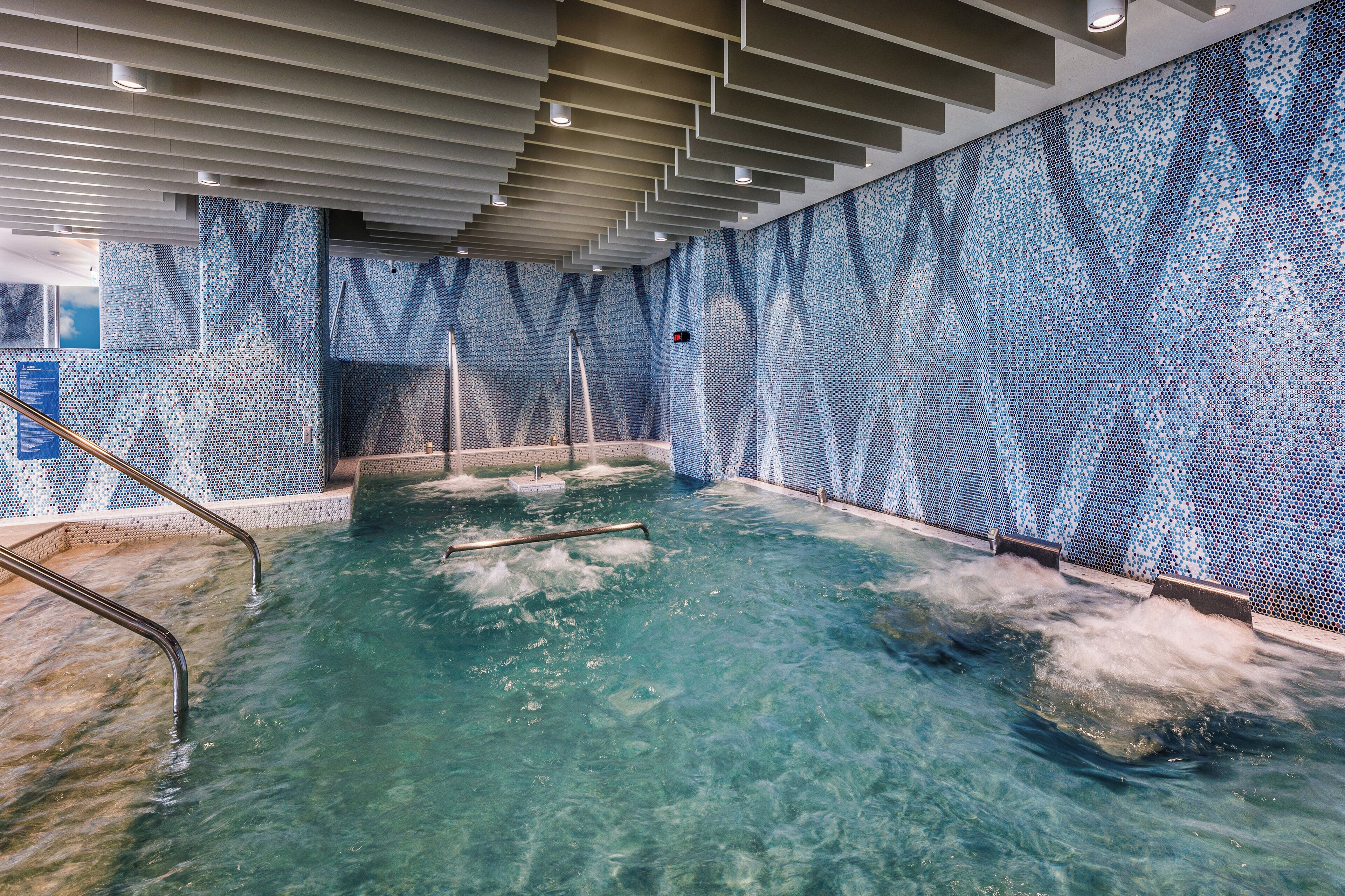 Una piscina con agua cristalina, rodeada por un muro de azulejos con un diseño azul.