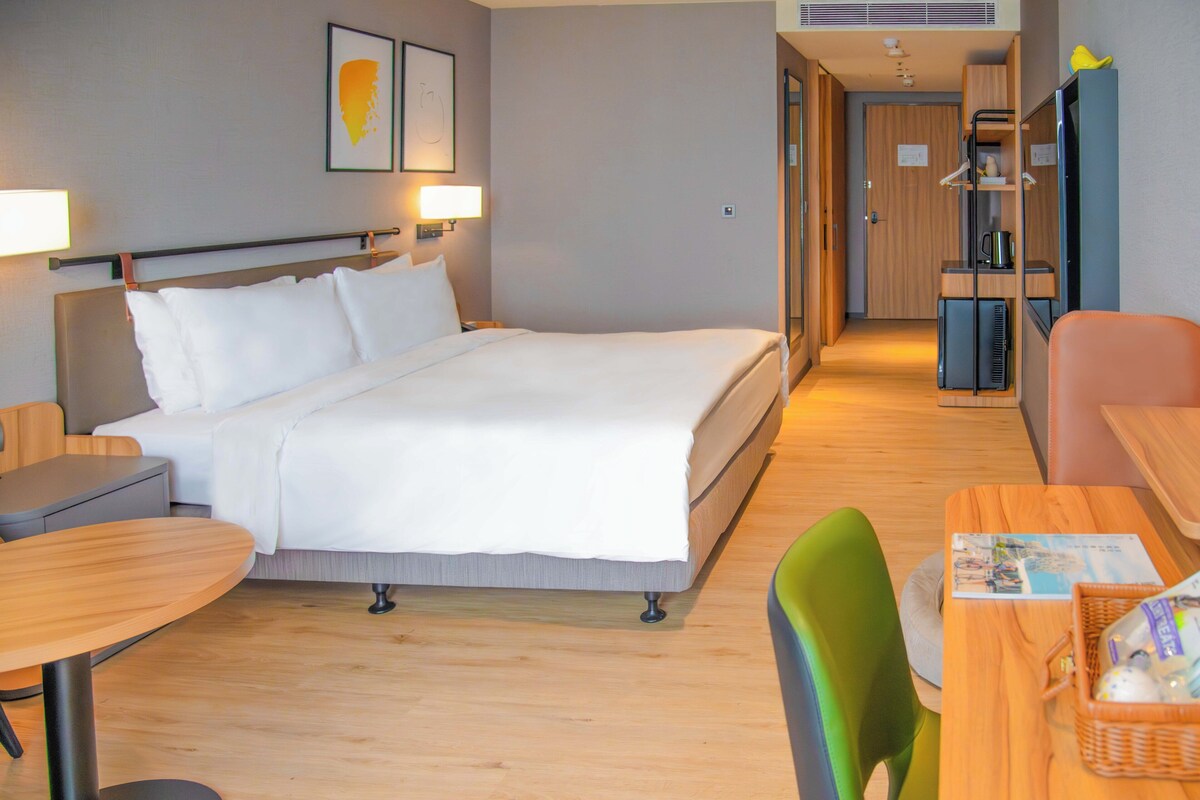A hotel room with a bed, a desk, a chair, a small table, and a TV.