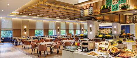 A spacious dining area with multiple tables and chairs, a central counter with food and beverages, and a decorative ceiling with wooden slats.