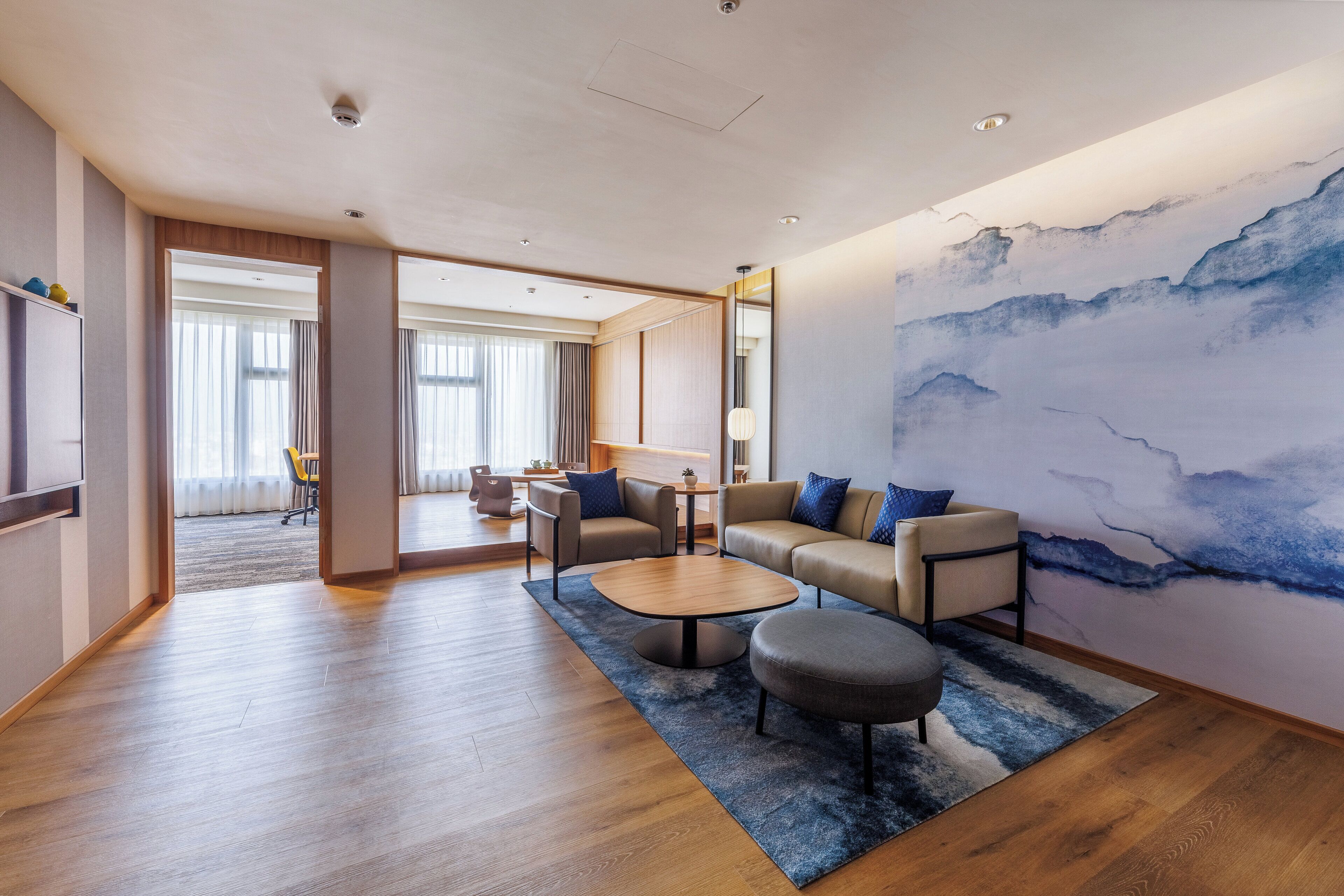 A modern living room with a sofa, coffee table, and ottoman, a large abstract painting on the wall, and a view into the dining area.