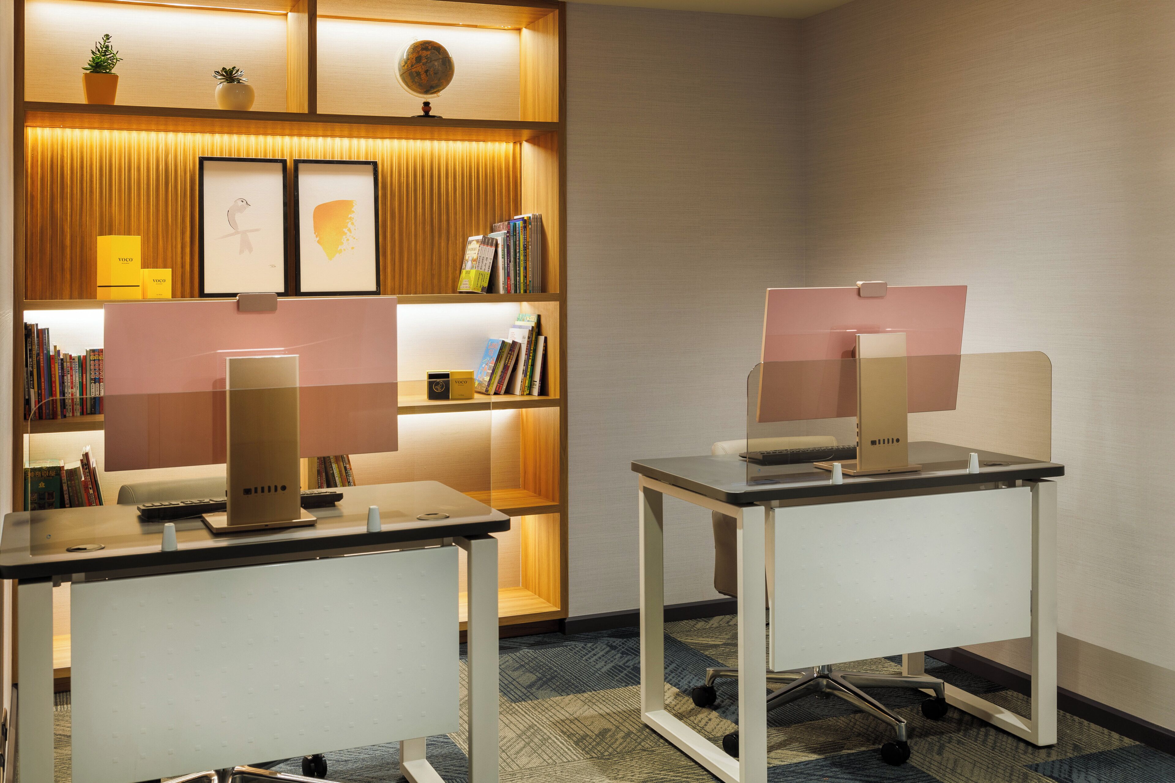 A modern office space with two desks, each with a computer and keyboard, and a bookshelf filled with books and decorative items.