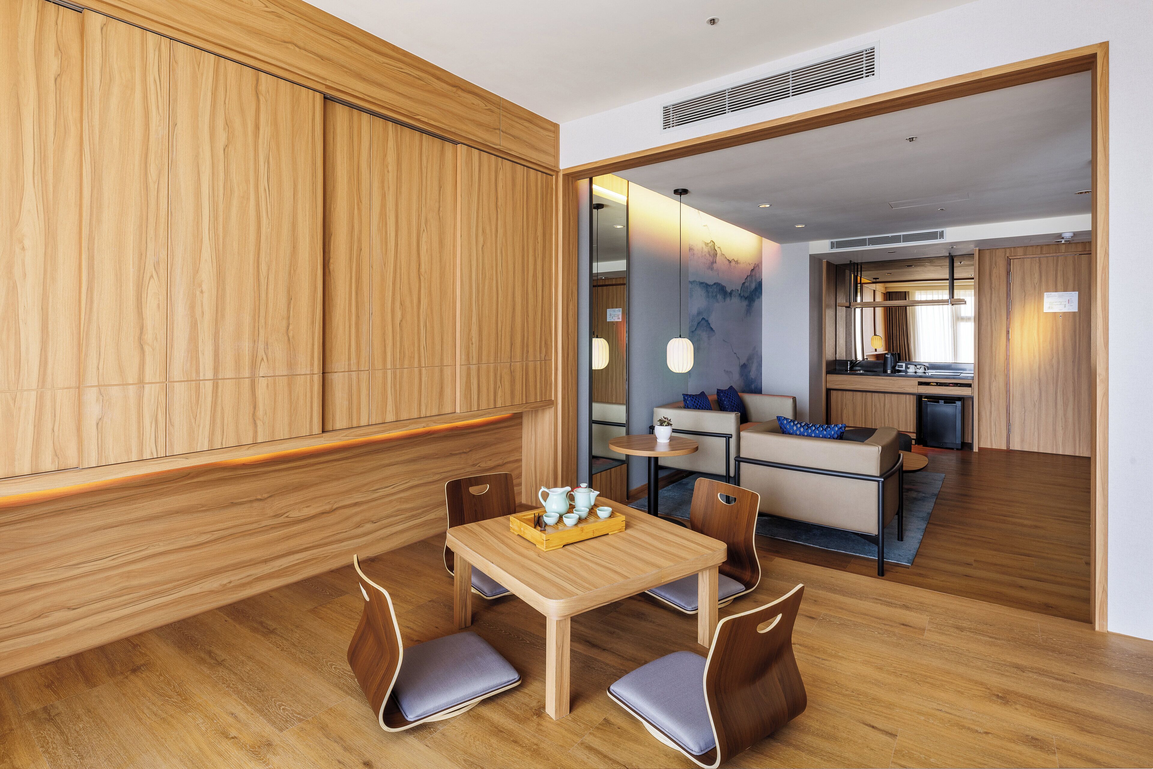 Una habitación de hotel moderna con una zona de comedor de madera, una kitchenette y una sala de estar con un sofá y una mesa de centro.