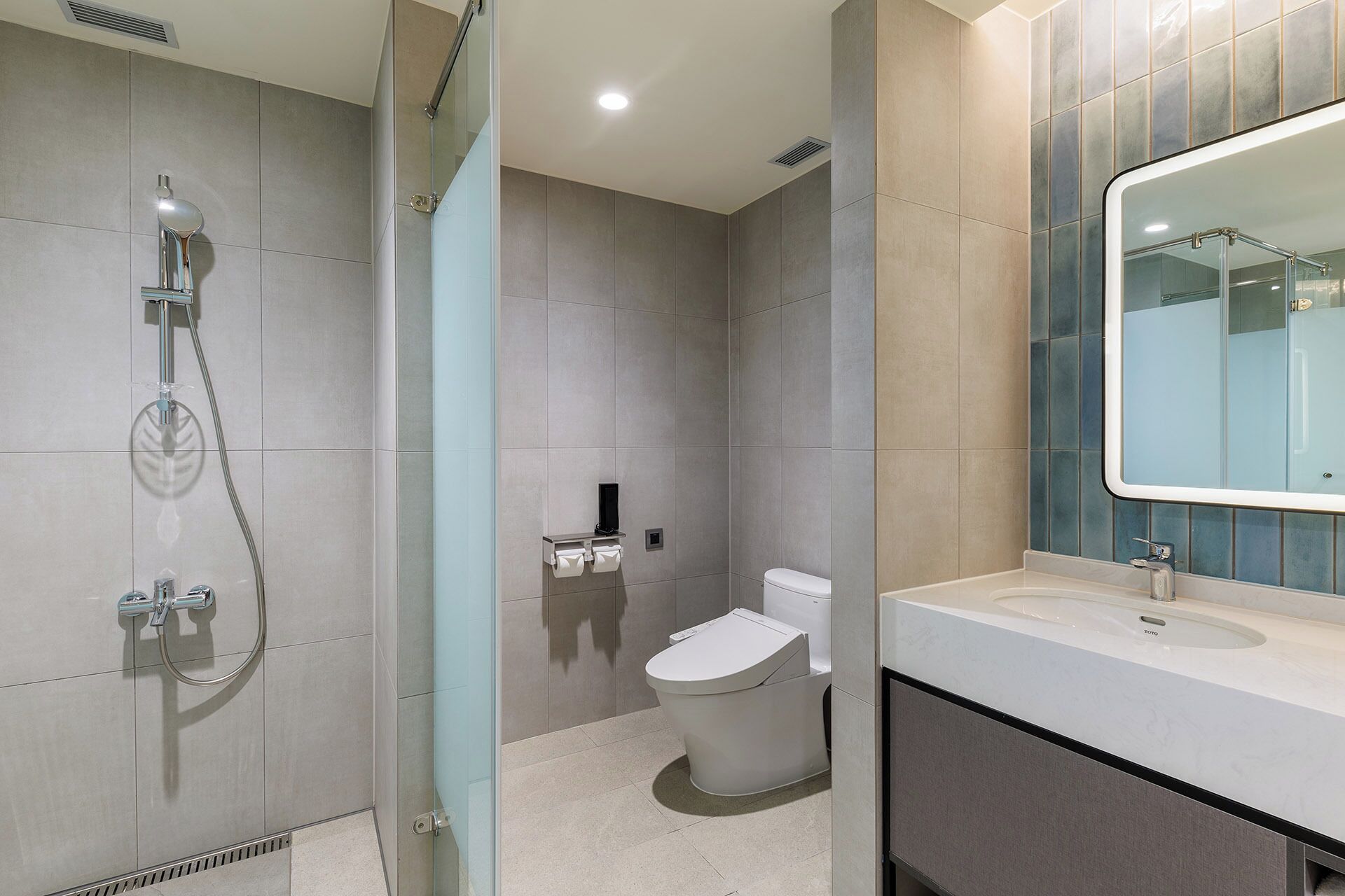 A modern bathroom with a glass-enclosed shower, a toilet, and a sink with a mirror.