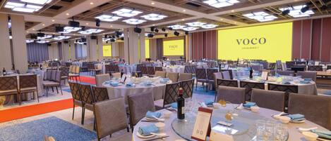 A conference room with multiple tables set for a meeting, equipped with microphones and a large screen displaying the word 'VOCO'.