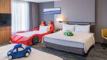 Ein Hotelzimmer mit einem großen Bett, einem kleineren Bett, einem Fernseher, einem Schreibtisch und einem Fenster mit Vorhängen.