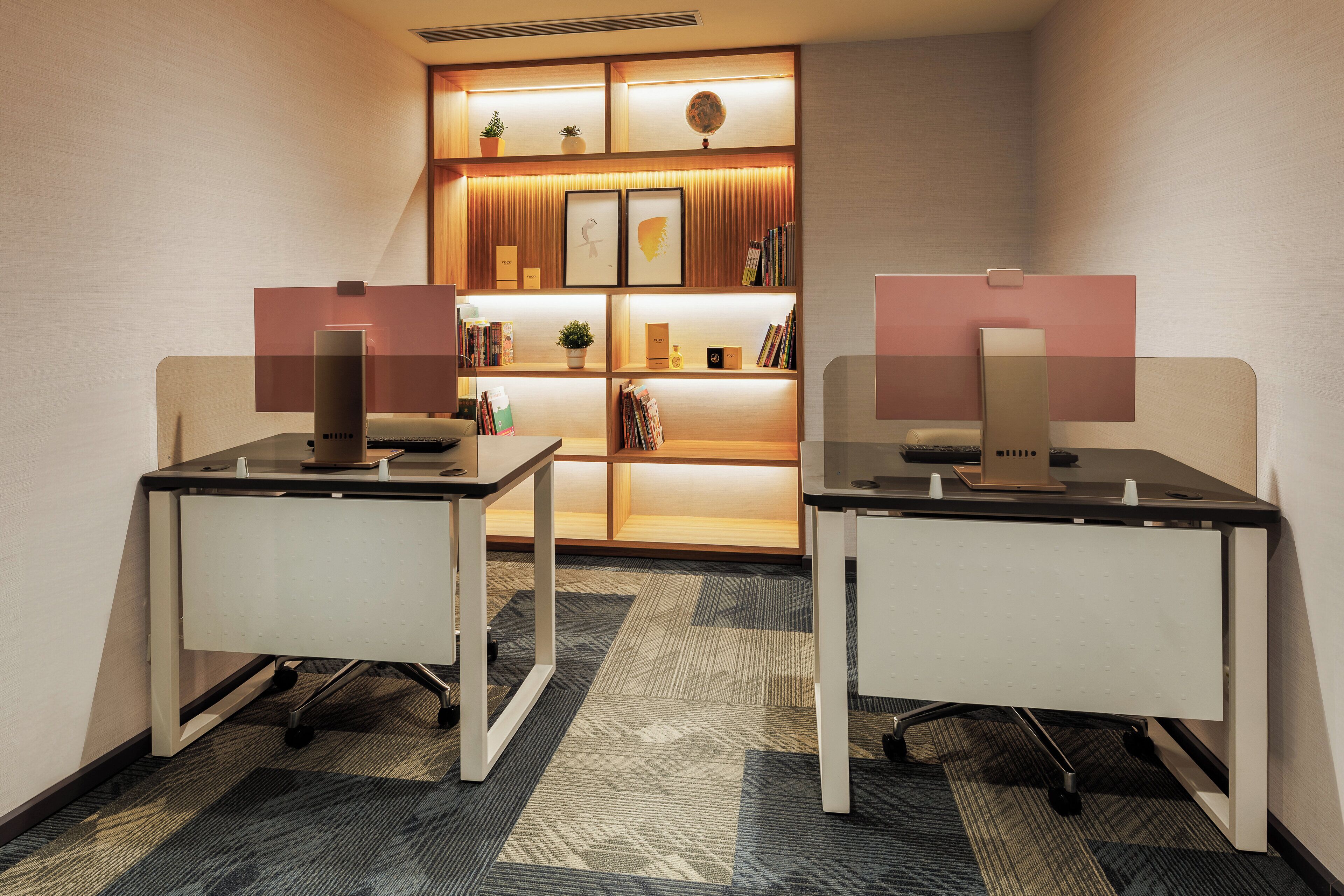 A modern office space with two desks, a bookshelf, and a decorative wall panel.