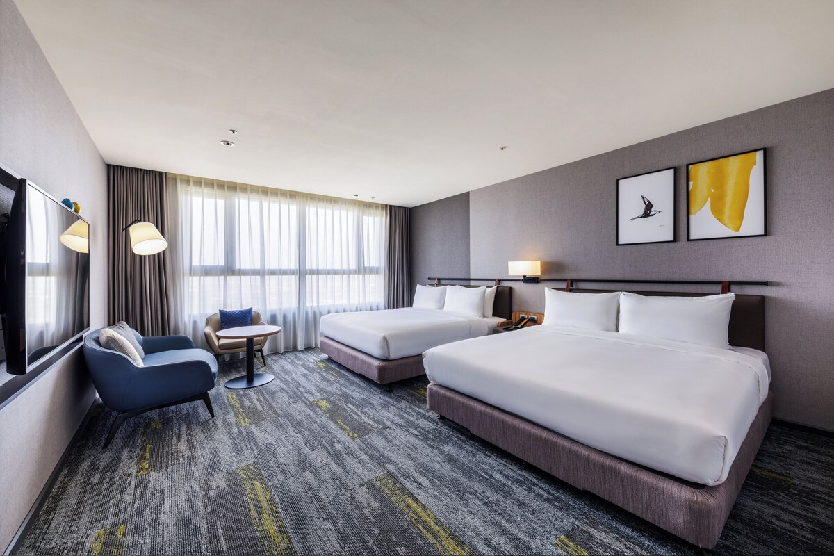A hotel room with two beds, a sofa, a small table, and a TV.