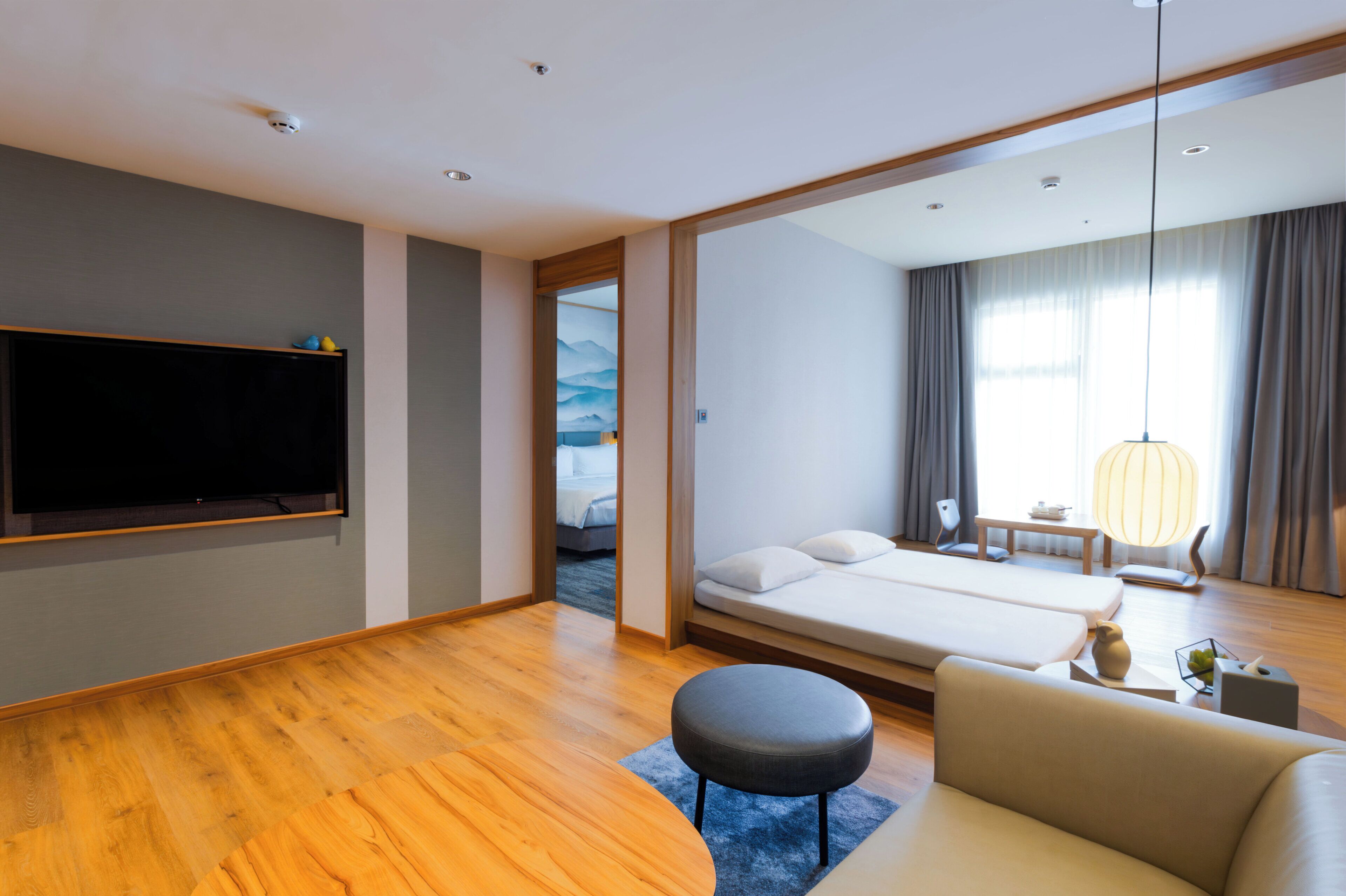 Une chambre d’hôtel moderne équipée d’un grand téléviseur à écran plat, d’un canapé, d’un lit, d’une petite table et d’une lampe.