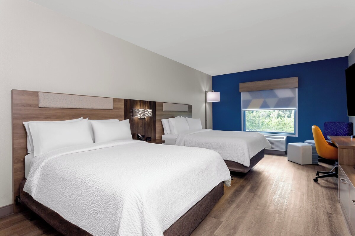 A hotel room with two beds, a desk, a chair, and a window with a view.