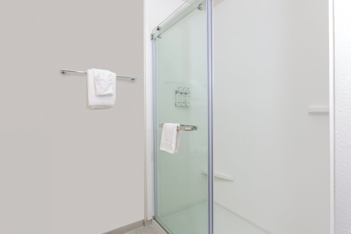A glass-enclosed shower with a towel rack and a small shelf with toiletries.
