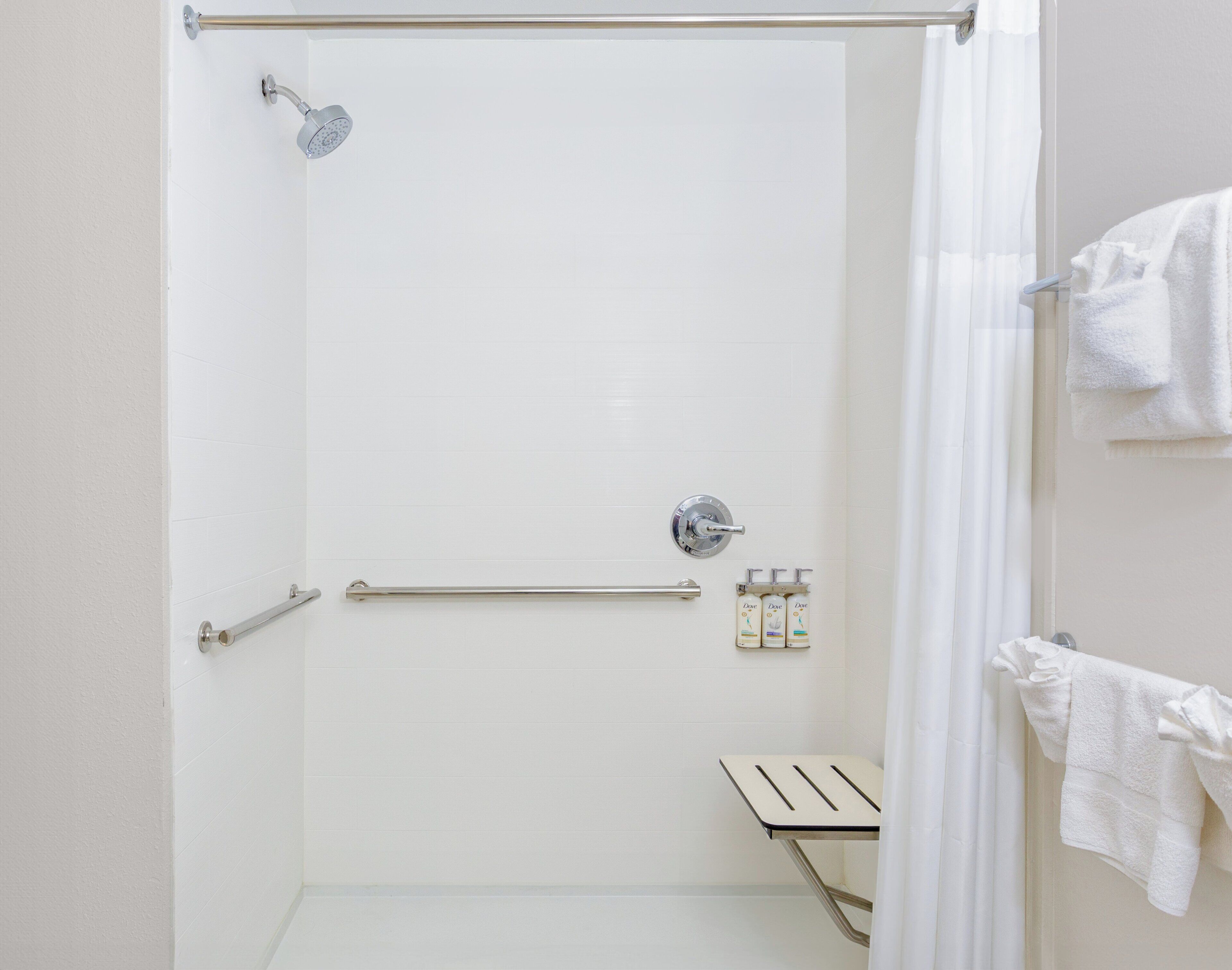 A walk-in shower with a handheld showerhead, a towel rack with towels, and a small shelf with toiletries.