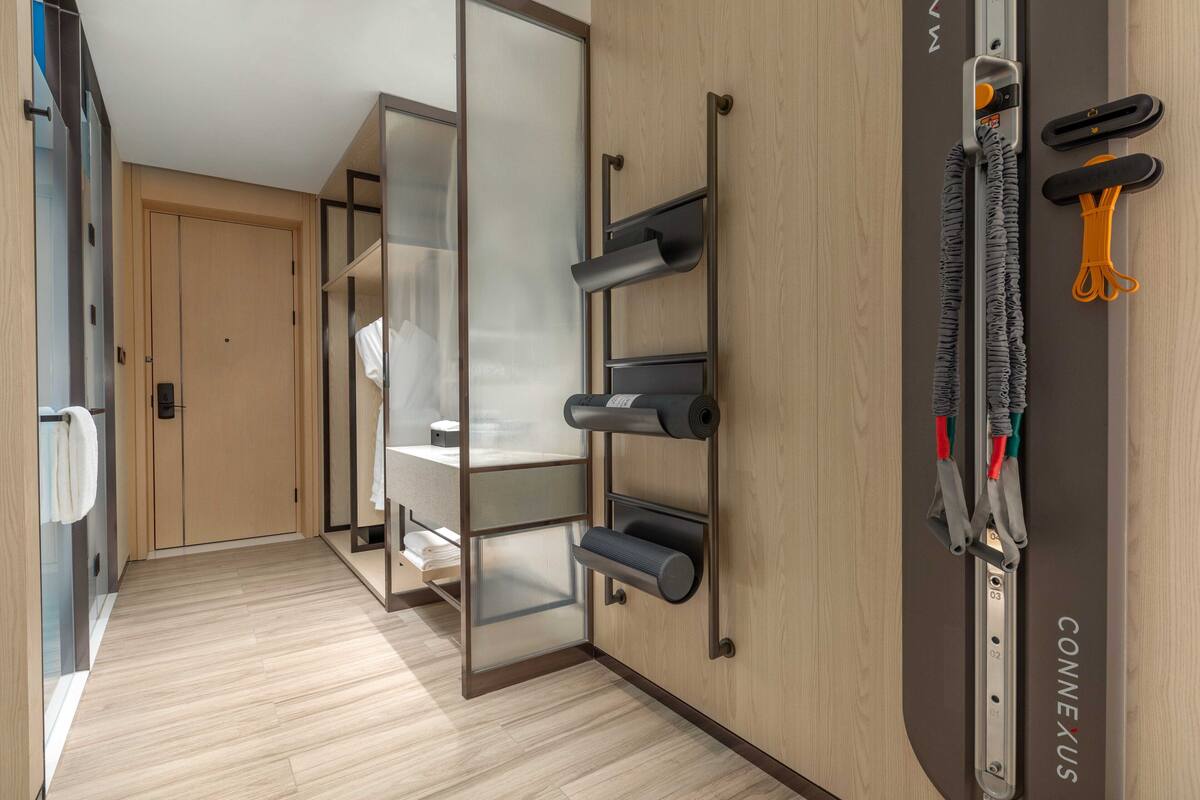 Une chambre d’hôtel moderne avec un plancher en bois, une porte-fenêtre coulissante donnant accès à la salle de bain et un porte-serviettes fixé au mur.