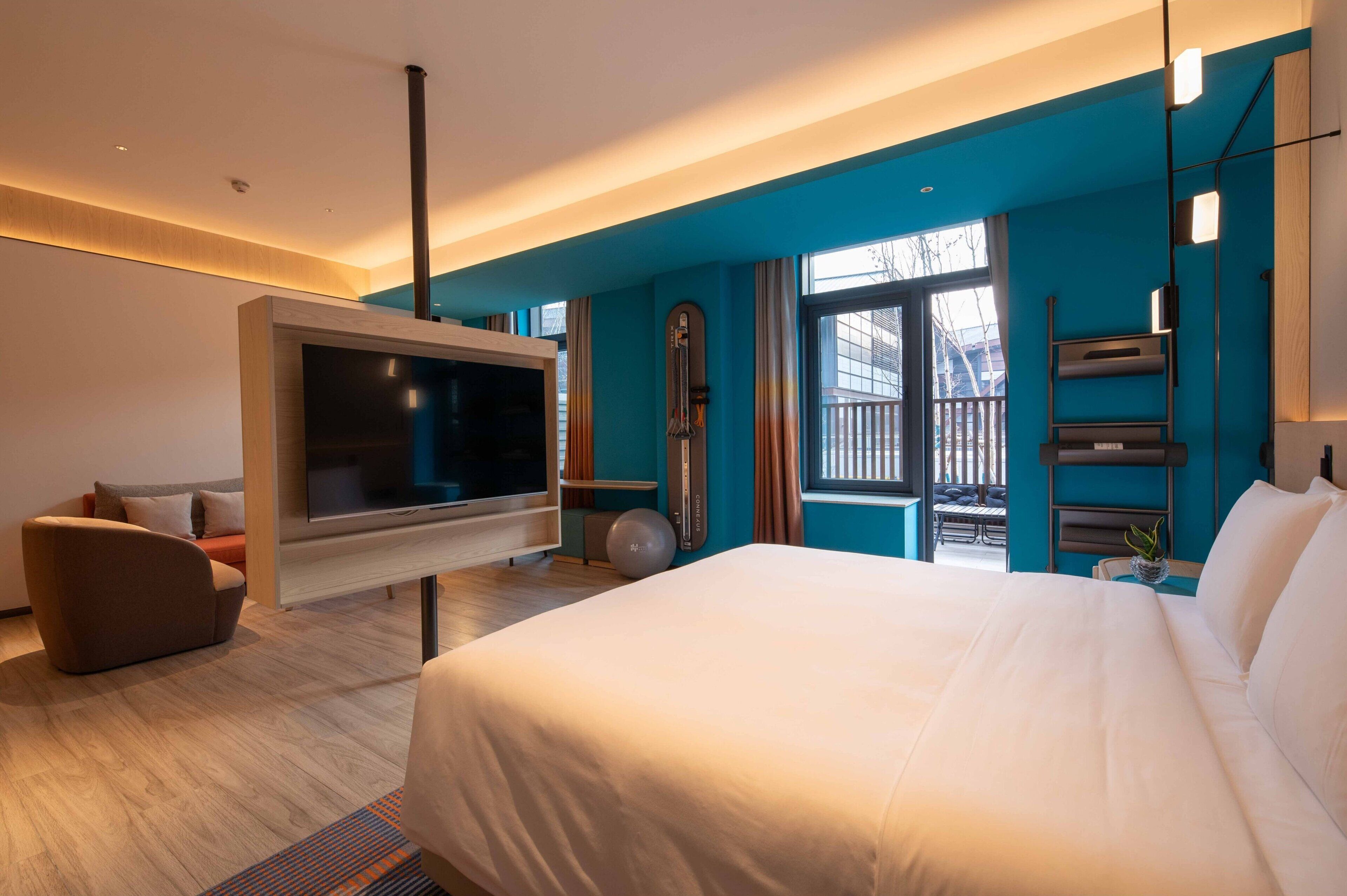 Une chambre d’hôtel moderne dotée d’un grand lit, d’un téléviseur à écran plat fixé au mur, d’un coin salon avec un canapé et d’une fenêtre donnant sur l’extérieur.