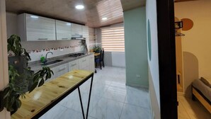 Una cocina compacta con armarios blancos, una mesa de madera y una ventana con persianas.