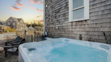 Un jacuzzi dans un jardin, avec une clôture en bois, une terrasse en bois et des maisons en arrière-plan.