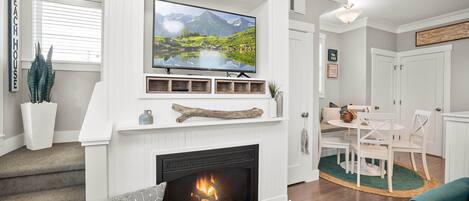 A living room with a fireplace, a mounted TV, and a dining area with white furniture.