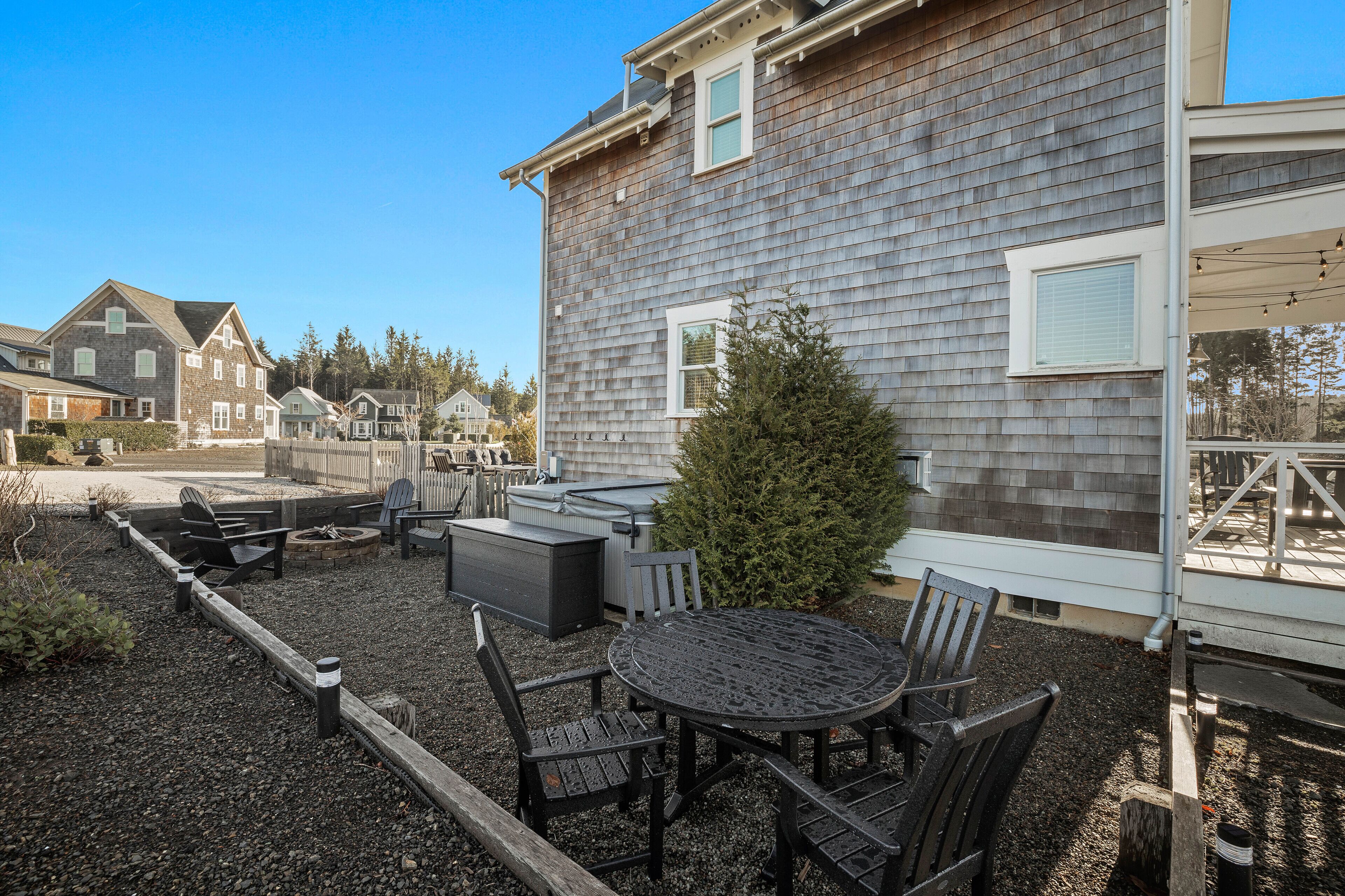 A patio area with a round table and chairs, a small fire pit, and a wooden fence.