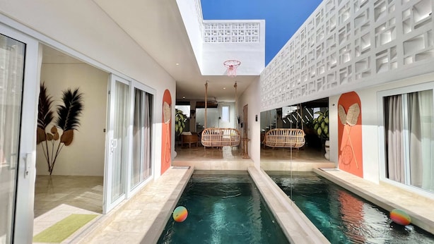 Una piscina interior moderna con agua cristalina, rodeada de puertas de vidrio y paredes blancas con diseños geométricos.