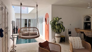 Un interior moderno con una silla colgante junto a una piscina, mobiliario de mimbre y una planta grande en maceta.