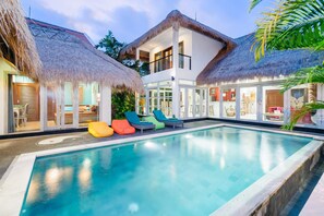 A modern poolside area with a clear pool, thatched-roof structures, and colorful lounge chairs. - Villa Sophie (Canggu)