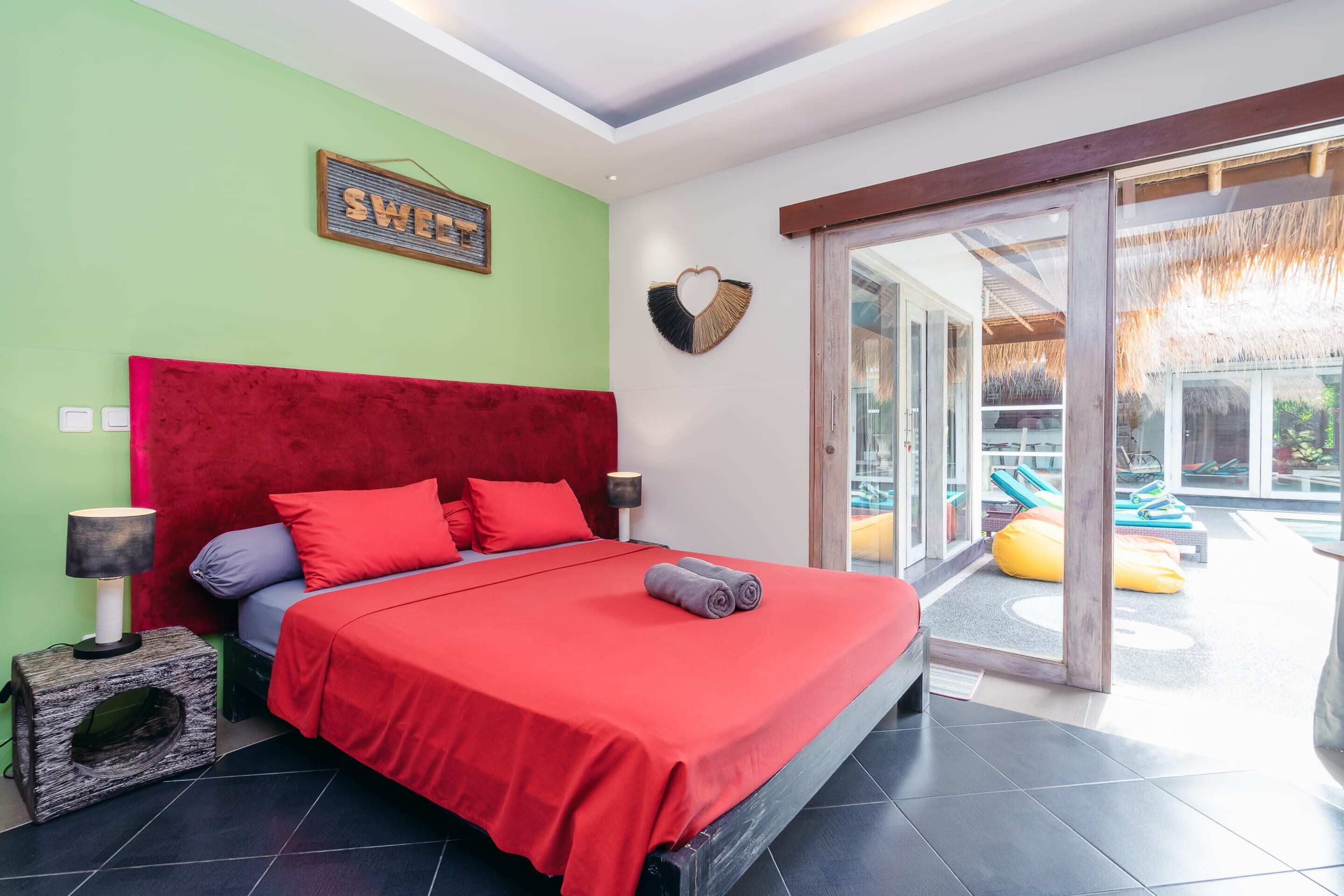 A modern bedroom with a red bedspread, a red headboard, and a green wall.
