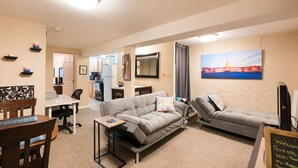 A living room with a sofa, a dining table, and a TV. There is a painting on the wall and a sign with information.