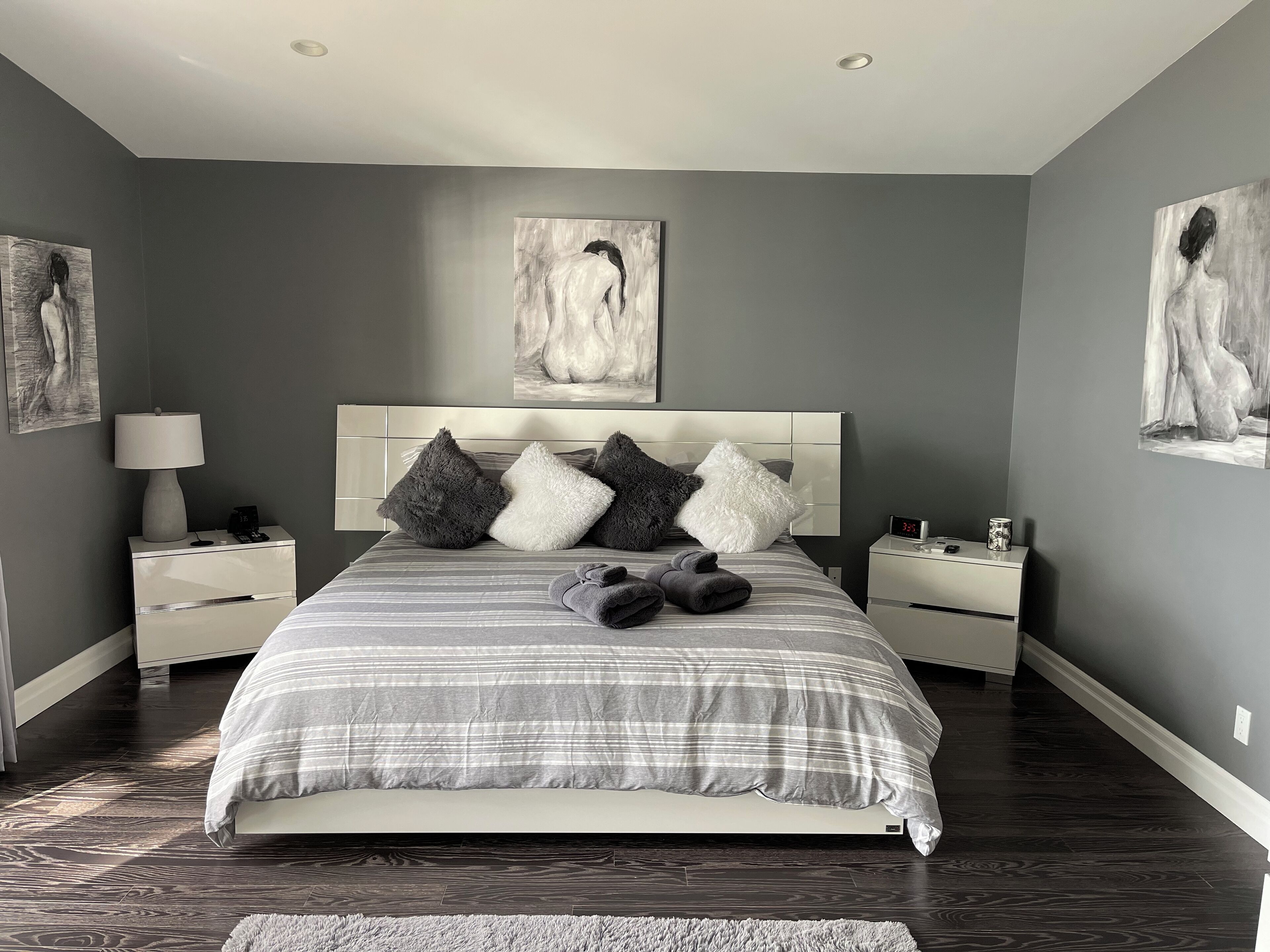 Ein modernes Schlafzimmer mit einem großen Bett, grauen Wänden und Kunstwerken.