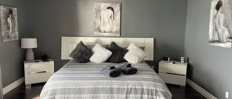 Ein modernes Schlafzimmer mit einem großen Bett, grauen Wänden und Kunstwerken.