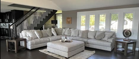 A modern living room with a sectional sofa, a wooden coffee table, and a staircase.