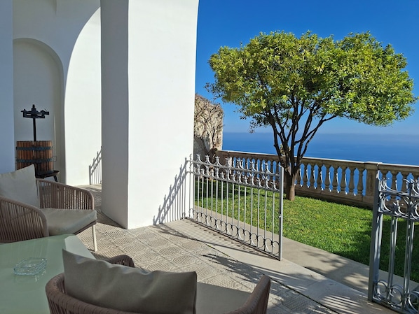 A balcony with a view of the sea, a tree, and a wrought iron railing.