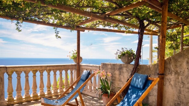 Eine Holzpergola mit Blick auf das Meer, zwei blaue Liegestühle und ein Blumentopf.