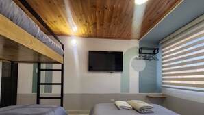 Ein Schlafsaalzimmer mit Etagenbetten, einem Fernseher, einem Wandregal und einem Fenster mit Jalousien.