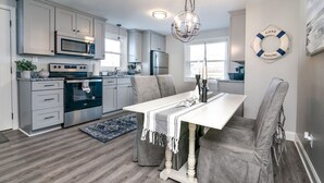 Een moderne keuken met grijze kastjes, roestvrijstalen apparatuur, een witte eettafel en een kroonluchter.