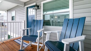 Een veranda met twee Adirondack-stoelen, een witte deur en een raam met luiken.