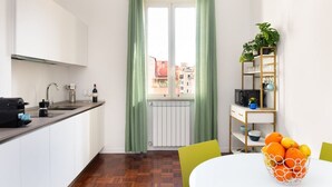 Eine kleine Küche mit Fenster, Heizkörper, Kaffeemaschine und einer Obstschale auf dem Tisch.