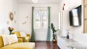 Ein modernes Wohnzimmer mit einem gelben Sofa, einem Glastisch und einem großen Fenster mit grünen Vorhängen.