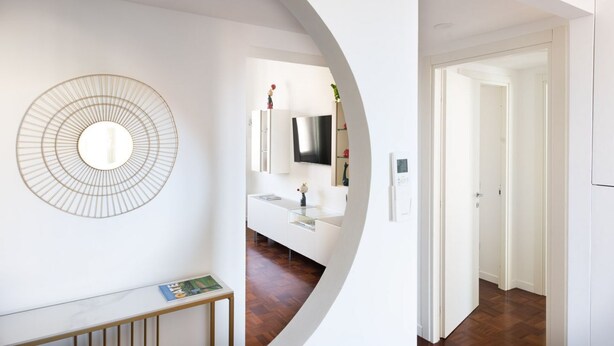 Ein modernes Interieur mit einem runden Wandbild, einem weißen Konsolentisch und einem Flur, der zu einer Tür führt.