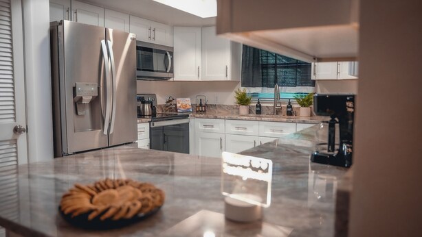 Una cocina moderna con electrodomésticos de acero inoxidable, muebles blancos y encimera de mármol.