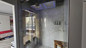 A modern bathroom with a glass shower enclosure, a marble wall, and a visible cityscape through the glass door.