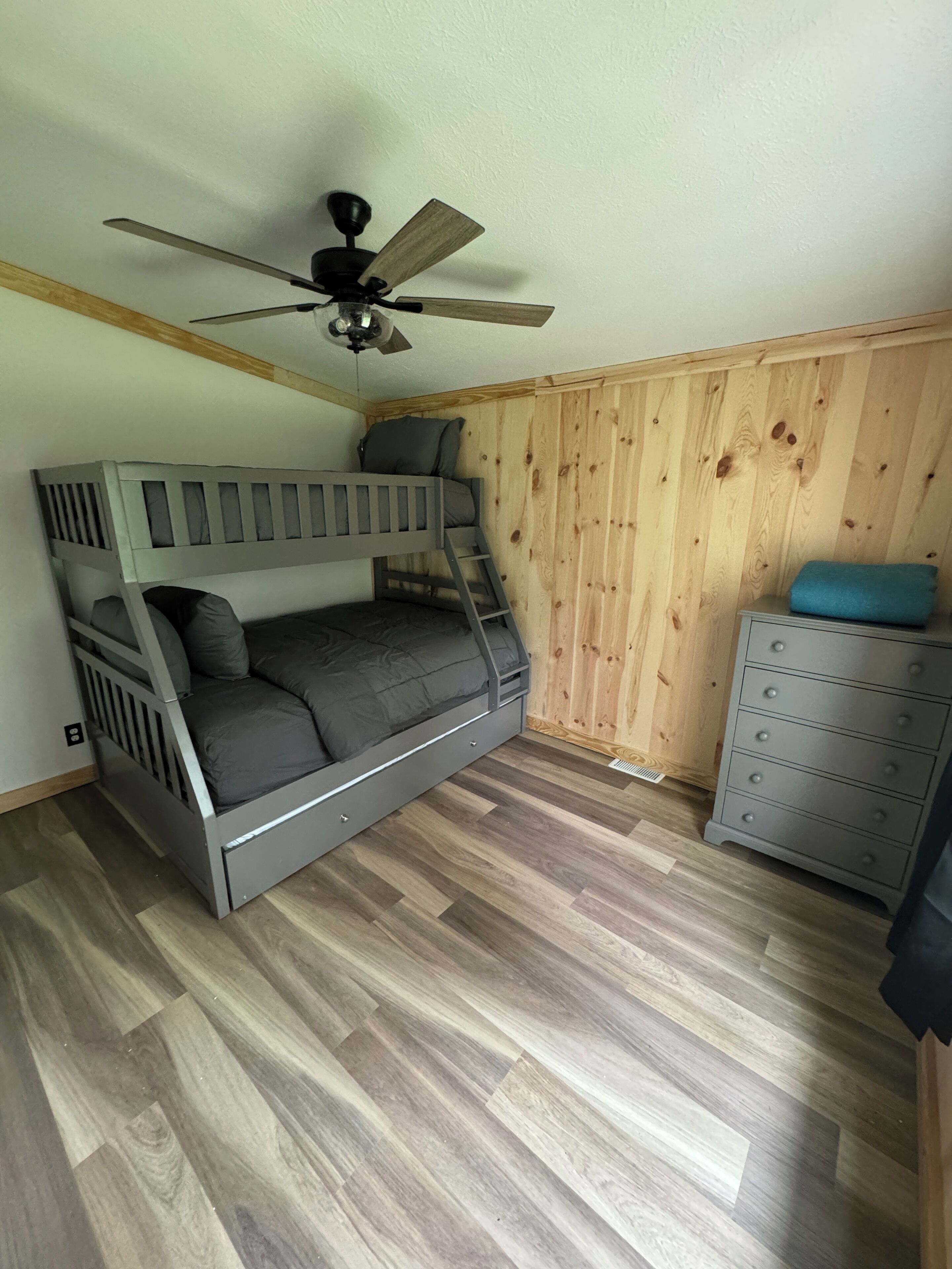 A bunk bed with a ladder, a ceiling fan, and a dresser with drawers.