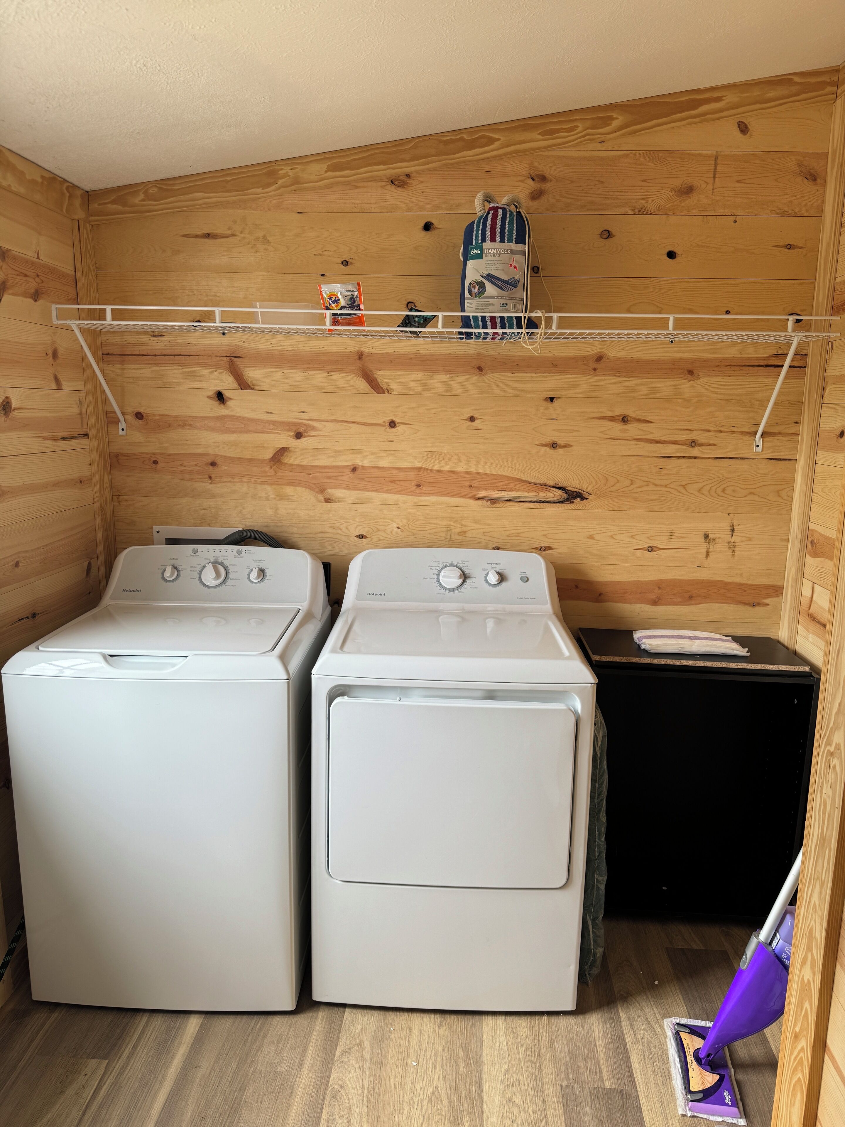 A laundry area with two front-loading washing machines, a drying rack, and a vacuum cleaner.
