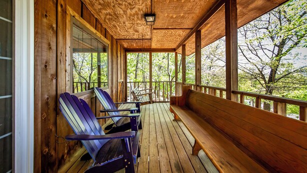 A wooden porch with a bench and Adirondack chairs, overlooking a forested area. - Blue Clouds Resort Hidden Gem! (Edgemont)