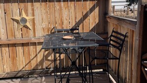 Een houten terras met een metalen tafel en stoelen, een sterversiering, en uitzicht op bomen en heuvels.